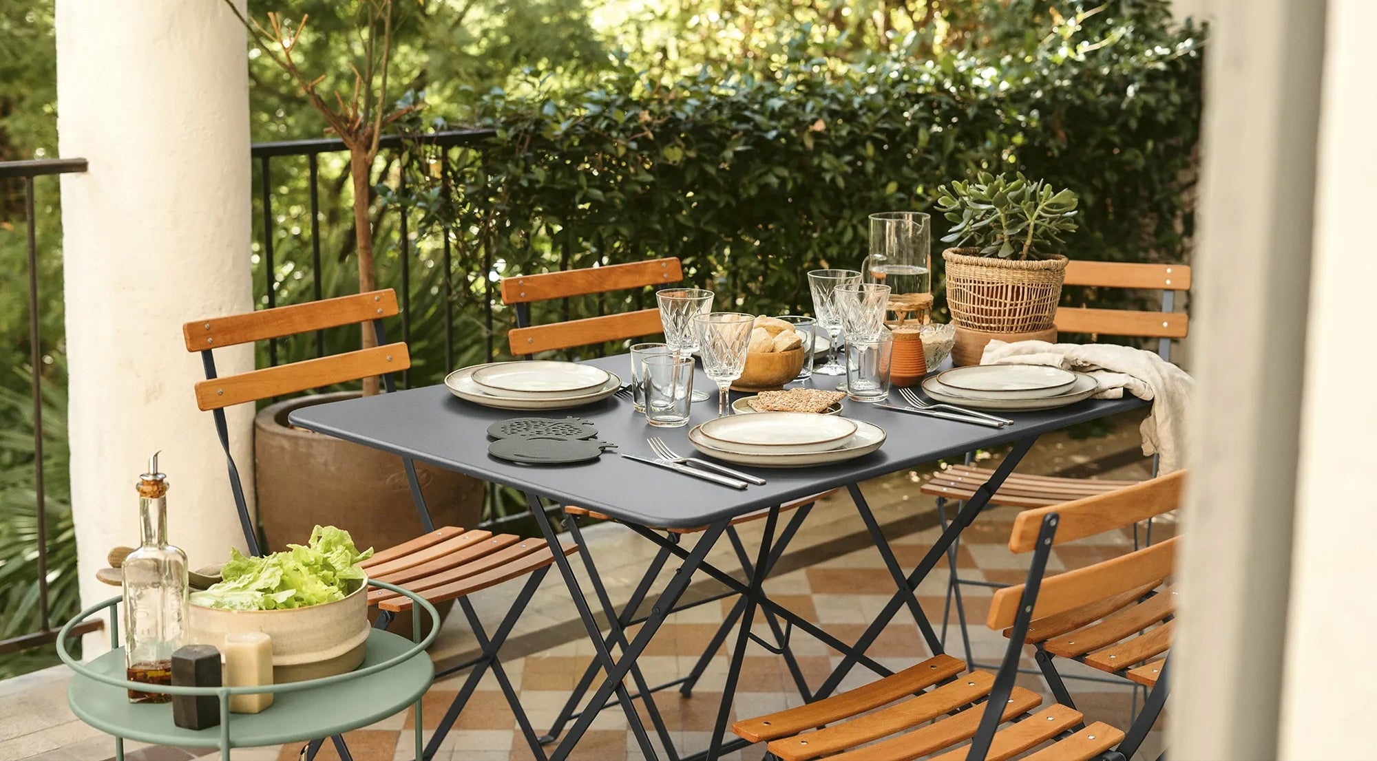 Fermob Outdoor dining setup with a table and chairs on a balcony with greenery.